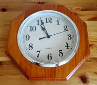 Front view of the quartz wall clock showing wooden octagonal frame, white face, black numerals, and silver bezel.