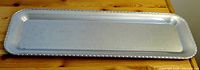Full length view of a long rectangular, chrome-plated metal tray with a scalloped edge.