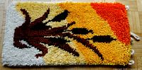 Full view of rectangular rya wall hanging with bullrushes design in shades of brown, black, white, yellow, and orange.