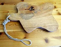 Front view of the solid wood cutting board with a rope handle, showing the natural wood grain and organic shape.