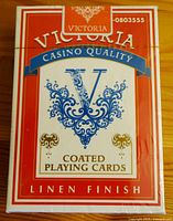 Front face of the unopened red and white box of Victoria Casino Quality coated playing cards with linen finish, showing decorative blue 'V' and gold motifs.