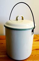 Front view of vintage white enamel cooking pot with lid and wire handle.
