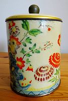 Side view of the metal container featuring floral decorations and yellow lid with green knob.
