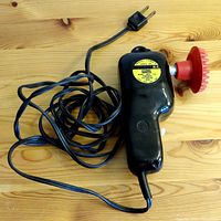 Black Wahl Mfg Co Hand-e Model electric handheld massager with visible power cord and plug on wooden surface.