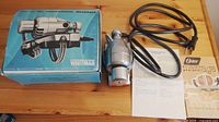 The electric handheld massager, its original blue Whitmar box, and a printed manual placed on a wooden surface.