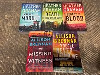 Five paperback novels laid on carpet, displaying front cover artwork and titles of suspense thrillers by Heather Graham and Allison Brennan.