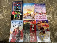 Front cover view of six holiday romance paperback books laid out on a wood surface: Snowcountry Christmas, My Kind of Christmas, The Sound of Sleighbells, Hero for the Holidays, All is Bright, Here Comes Cowboy Claus.