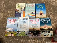 Front view of all 7 paperback books arranged on wooden floor showing covers by Brenda Novak and Danielle Steel.