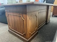 Side view of antique wooden desk showing embossed panel design and glossy brown wood finish.