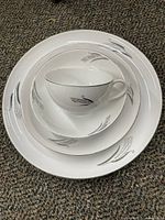 Stacked grouping of smaller and larger bowls with a teacup and saucer on top showcasing silver edged floral design on white porcelain.