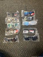 Overview of 10 sunglasses individually packaged in plastic, showcasing variety in frame colors and lens types including blue reflective, clear, and tinted lenses.