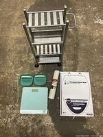 Photo showing all items in the lot: metal organizing rack, green soap holders, digital scale, shower mat, and boxed toilet seat.