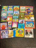 Overview of 26 children's books arranged on floor showing covers with colorful illustrations and titles.