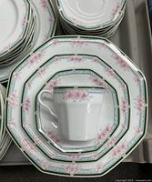 Close-up photo showing the fine china's octagonal shape with pink floral pattern, green decorative band, and gold trim. Tea cup placed on a small plate to show matching design.