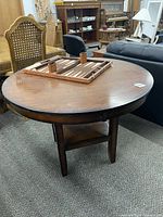 Round wooden table with dark brown finish shown from top view, revealing some scuffs and scratches and a backgammon game set on top.