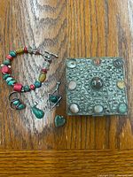 Top-down view of the jewelry lot including bracelet, rings, pendants, and decorative box on wood surface.