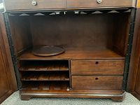 Interior view of cabinet with doors open showing shelves, built-in wine rack holding 12 bottles horizontally, two drawers inside, and a lazy Susan circular wooden tray on the shelf.