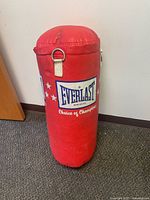 Front view of the red Everlast canvas punching bag standing upright against the wall showing logo and wear.