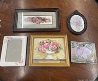 Five assorted decorative picture frames with floral designs arranged on a wooden surface. Frames include a dark brown rectangular, an oval dark brown, a white rectangular, a wooden rectangular, and a pastel floral frame.