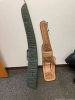 Full view of green GunMate canvas gun case and custom embossed leather gun case side by side against wall and floor.