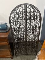 Front view of the closed brown iron wine rack with scrollwork design and arched top.