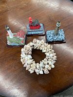 Top view showing one circular natural seashell wreath and three distinct lighthouse figurines placed on a wooden surface.