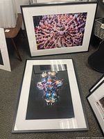 Two framed photographs by Ron Cooper displayed on floor: one showing circular group performance, other a colorful abstract figure. Both have black frames and white matting.