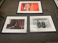Three framed photographs arranged on carpet: one portrait with orange background, one indoor scene with an elderly woman, one black and white of two men.