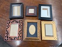 Top-down view of six picture frames with varied rustic and classic styles on a wooden surface.