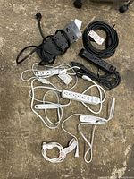 Seven assorted power strips arranged on floor, showing black and white units, various sizes, cords, and USB charging ports.