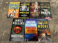 View of front covers of seven thriller books featuring authors Brad Thor, Lee Child and Andrew Child, Brad Taylor, Nelson DeMille, James Rollins, Jonathan Kellerman, and Taylor Moore.