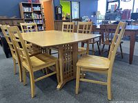 Angle view of traditional rectangular wood dining table with six matching chairs around it. Light wood finish and central pedestal base visible.