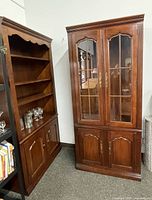 Two wood cabinets side by side, one with glass doors and shelves, other with shelves and lower storage