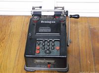 Front view of the black antique Remington Rand adding machine showing the manual crank, numeric keypad, and result window.
