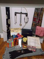Wide view of assorted ladies accessories including scarves, handbags, jewelry, gloves and other small items laid out on floor and hung on backdrop.