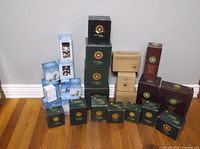 Photo showing multiple Boyds Bears boxes stacked on a wood floor against a white wall. Boxes are of various sizes and colors (green, blue, brown), some with windows showing small bear figurines inside.