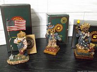 Three Boyds Bears patriotic bear figurines displayed with their original boxes: Uncle Elliot with flag, Ms. Libearty Statue of Liberty bear, and Sammy Bearamerican Uncle Sam bear.