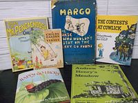 Photo showing all six children's hardcover books, arranged on a white wooden surface, titles visible