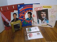 Overview of the lot showing 3 Elvis albums, socks in package, and 2 stamp first day covers on a wooden surface.