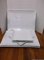 Stacked view of 3 large white rectangular platters and 2 square plates, showing size difference and shape.