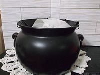 Black matte cauldron on a crocheted mat with a white background.