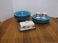 Set of 4 teal blue bowls, 4 dinner plates with scalloped edges stacked, ceramic butter dish with white lid and floral decoration.
