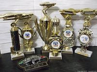 Full view of all 7 trophies arranged in a row, featuring cars and club logos on bases.