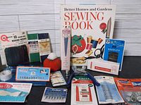 Photo of Better Homes and Gardens Sewing Book 1970 edition with various vintage sewing accessories including needles, pins, patches, and mini-stitcher