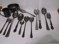 Photo showing 14 assorted silver plated utensils and serving pieces depicting forks, spoons, ladles, and a knife with decorative handles, some with pierced designs.