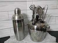 Photo of the vintage barware set displaying the stainless steel ice bucket filled with the bar utensils and the standalone cocktail shaker next to it.