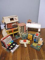 Full grouping of all 8 vintage Fisher Price Little People toys on floor, showing various playsets and accessories including elevator, Ferris wheel, cash register, and house.
