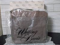 Plum/taupe mesh purse visible inside plastic packaging with Whiting and Davis printed box in background.