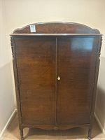 Front view of vintage solid wood armoire with two closed doors and decorative top edge.