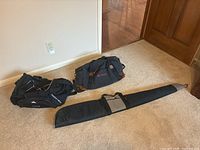 Two duffel bags and one soft rifle case on carpet near wooden door and hardwood floor